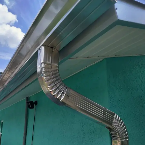 Custom bent aluminum downspout on a teal stucco home
